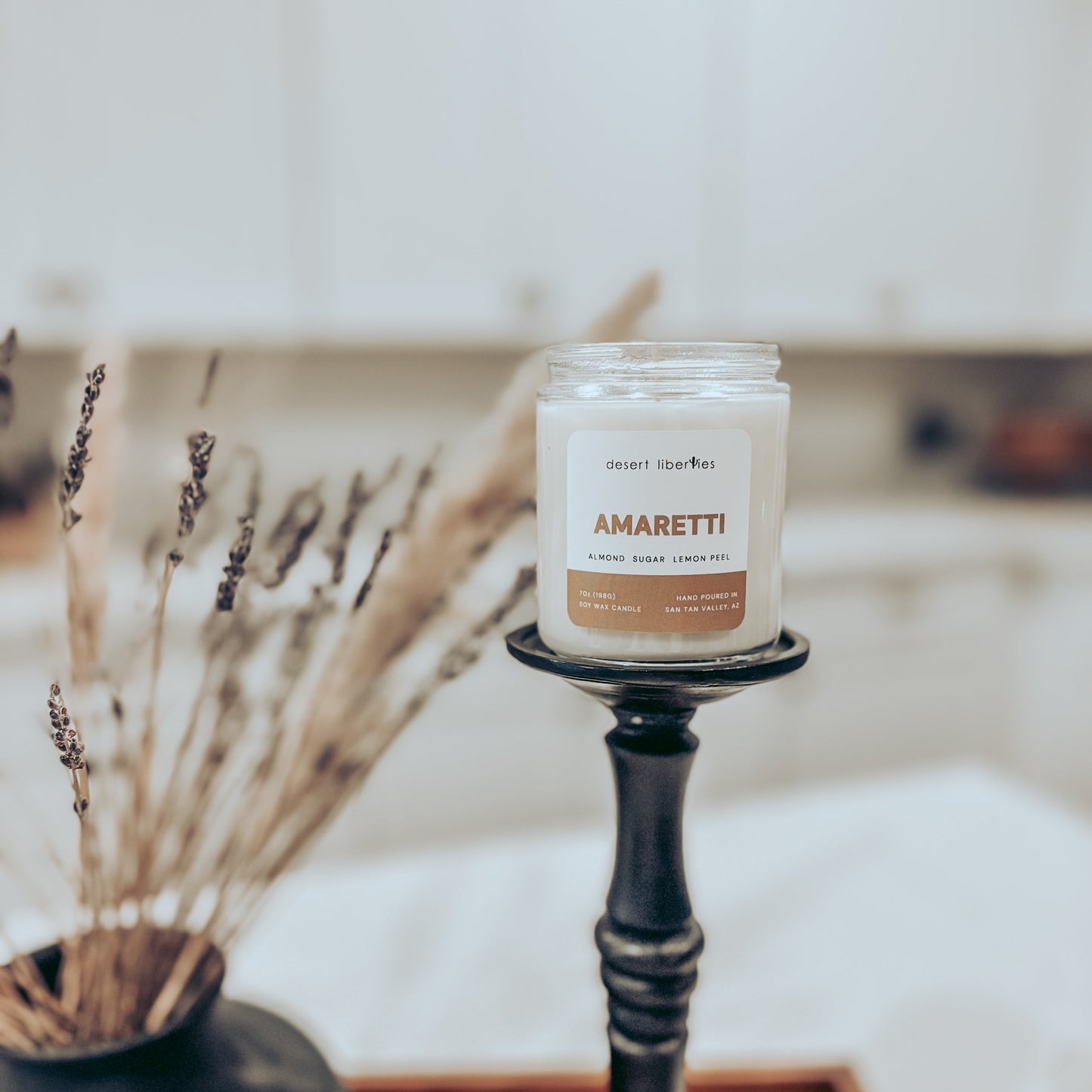 Candle labeled 'Amaretti' on a black holder with dried plants in the background