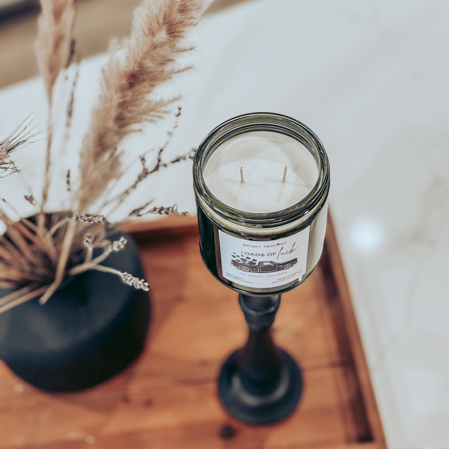 Candle in a glass jar on a wooden tray with dried plants