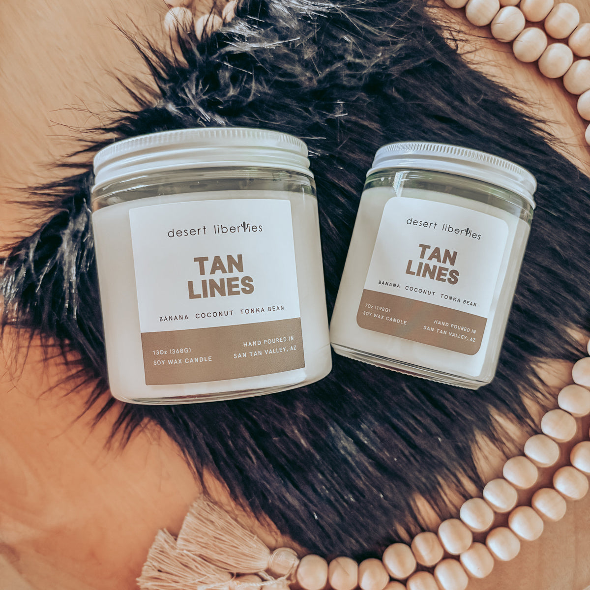 Two jars of 'Tan Lines' product on a fur surface with beads in the background.