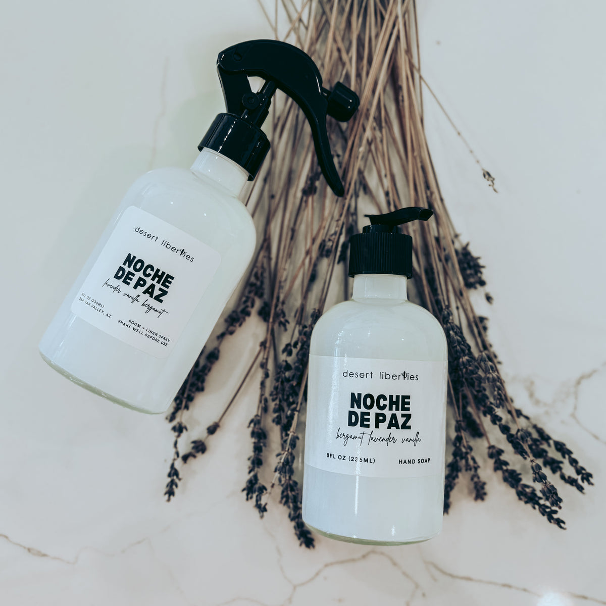 Two bottles of 'Noche de Paz' on a textured surface with dried lavender.