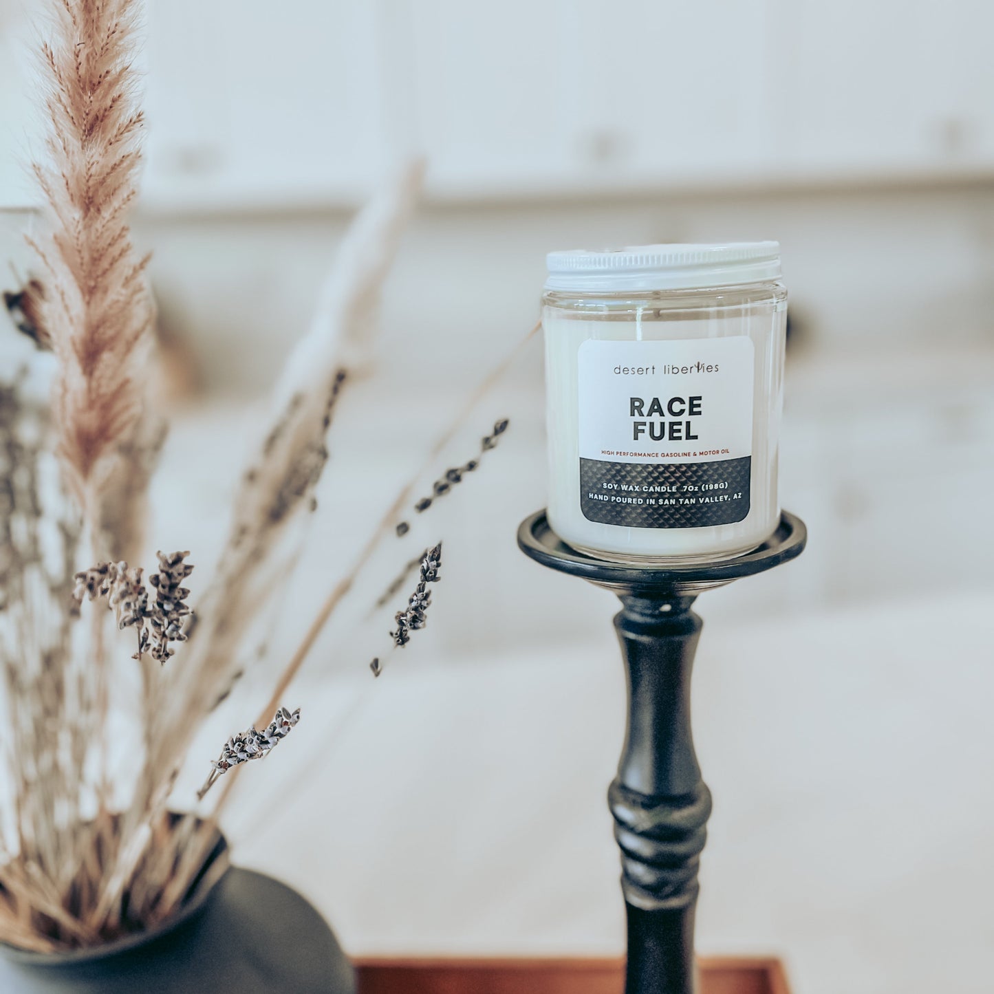 Race fuel scented candle on a black candlestick and blurred kitchen background.