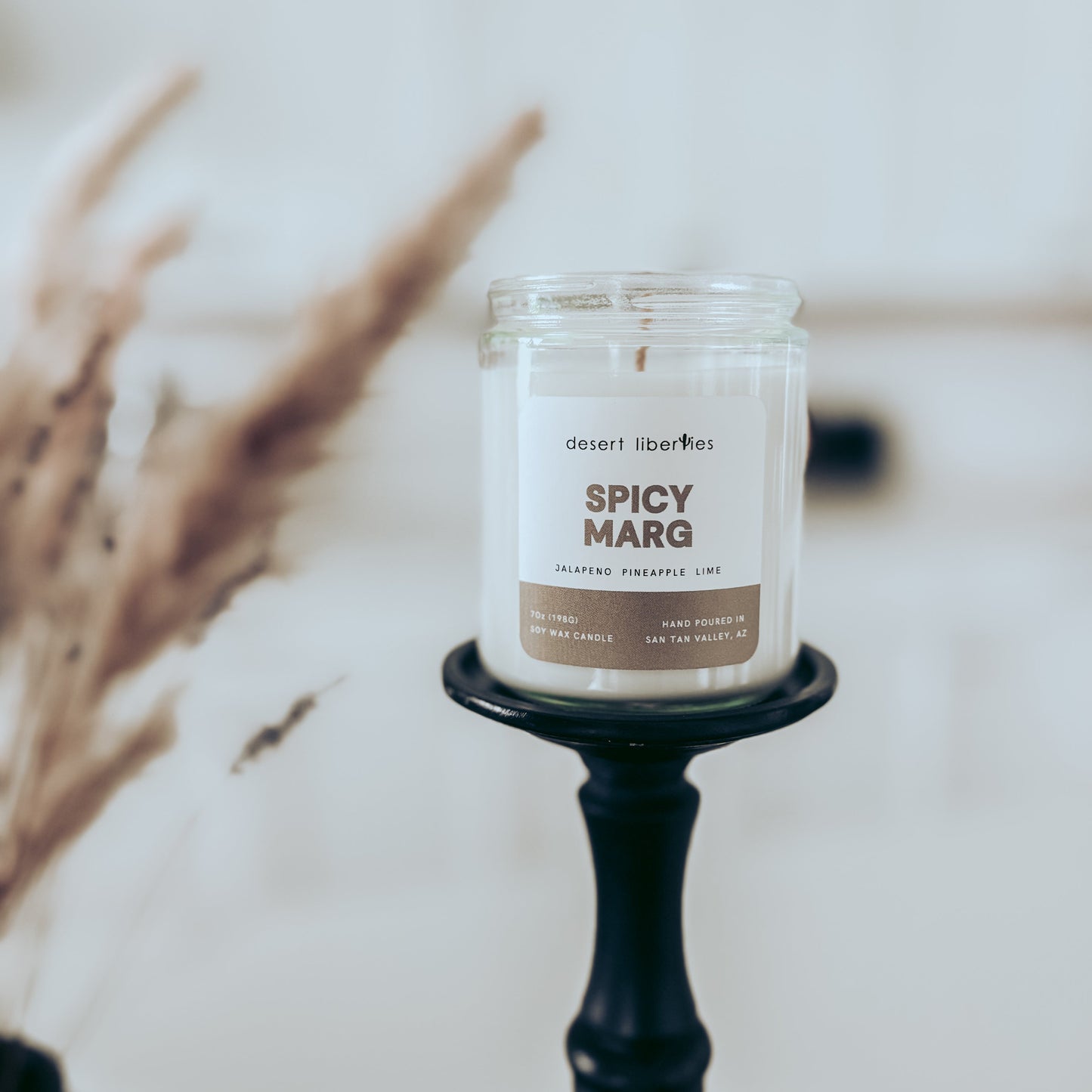 Candle labeled 'Spicy Marg' on a black holder with blurred background