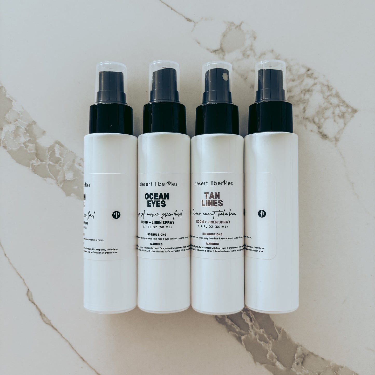 Four white spray bottles with black nozzles on a marble surface