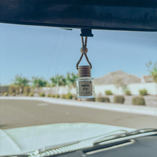 Load image into Gallery viewer, Car air freshener hanging from a car's rearview mirror with a desert landscape in the background.