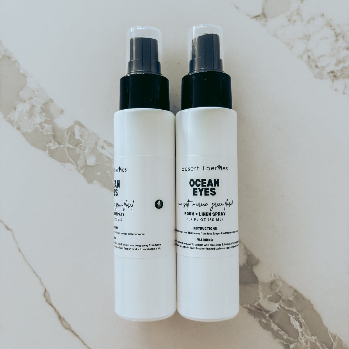 Two white spray bottles with labels on a marble surface