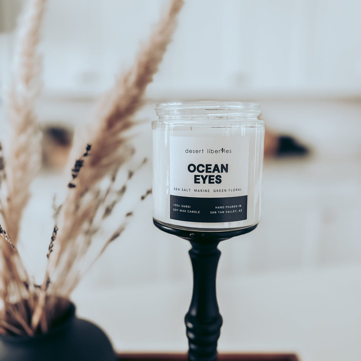 Candle labeled 'Ocean Eyes' on a stand with dried plants in the background
