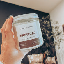 Load image into Gallery viewer, Hand holding a 'Nightcap' candle jar with a blurred indoor background