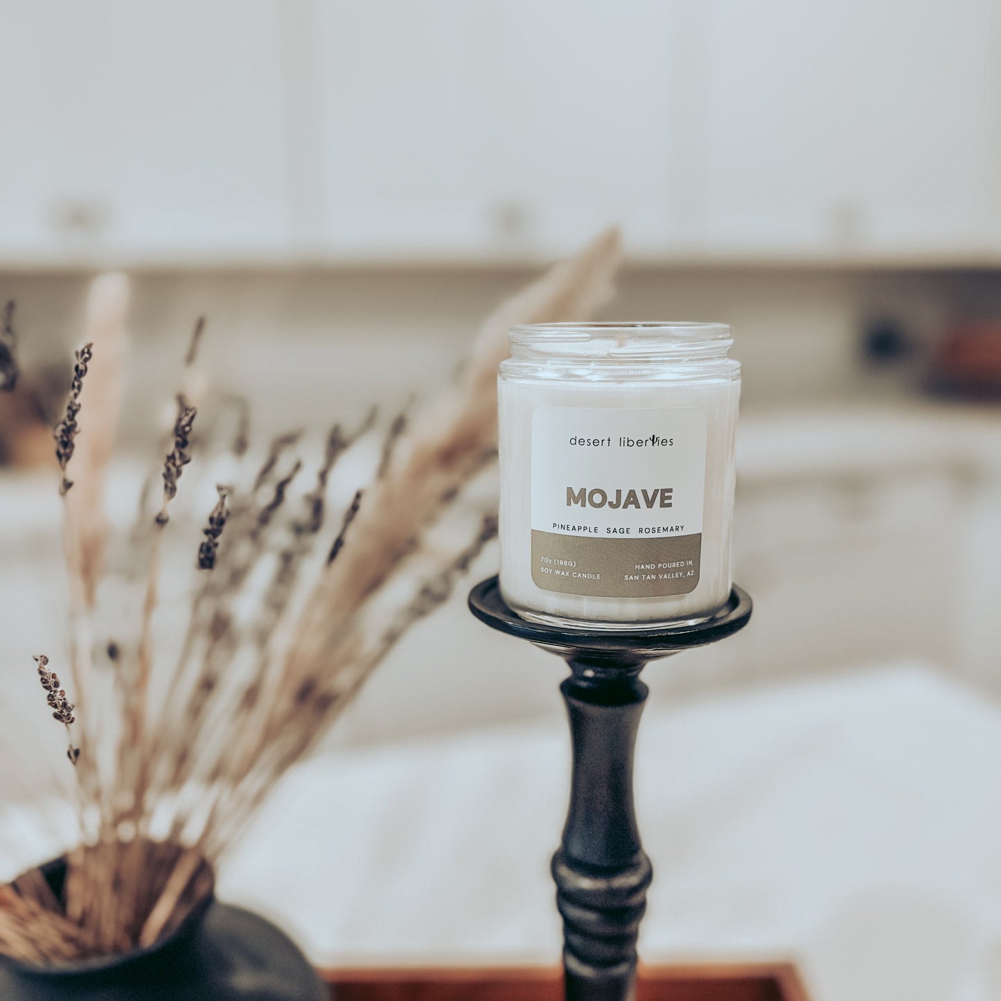 Candle labeled 'Mojave' on a black candlestick with dried plants in the background.