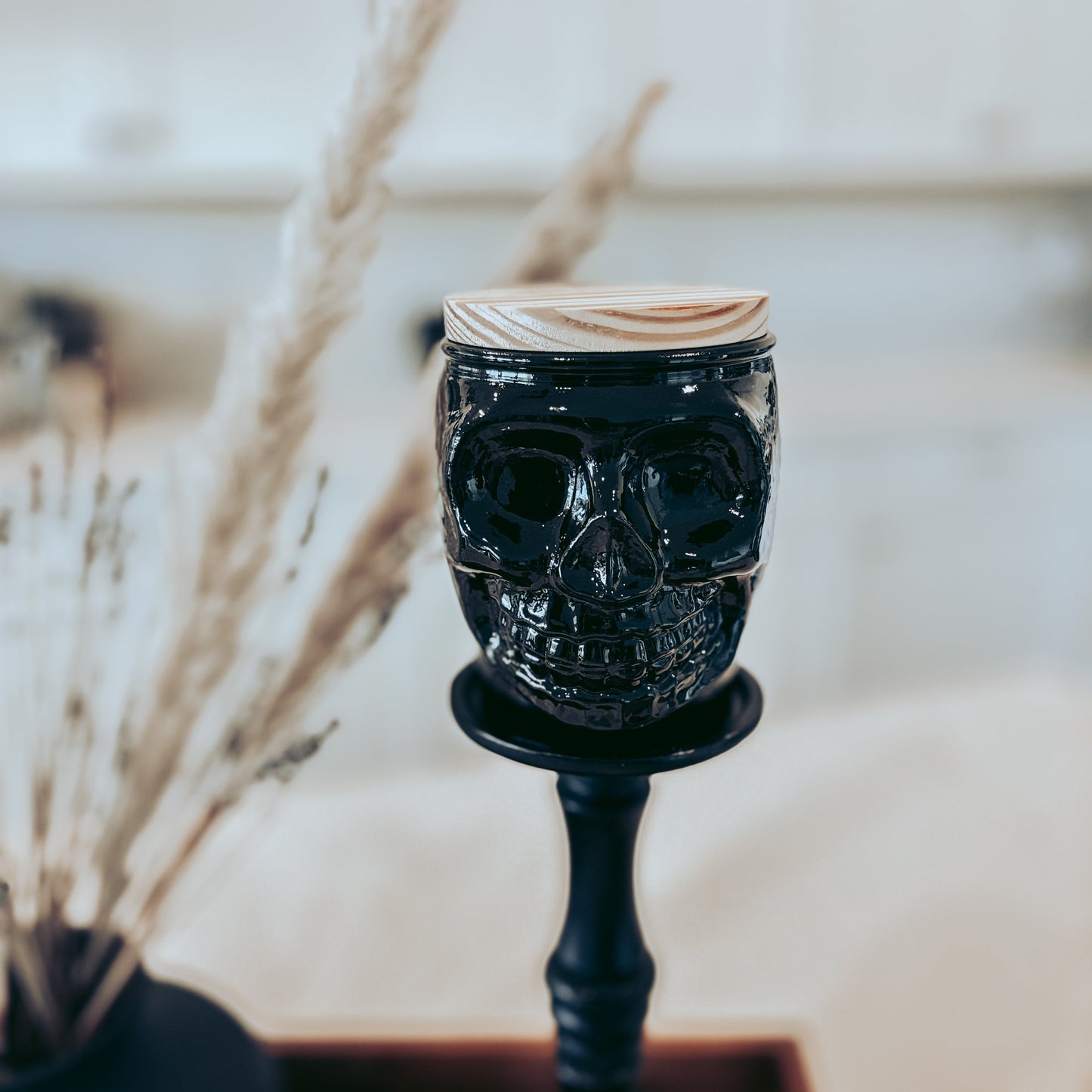 Black skull-shaped candle holder on a wooden surface with a blurred background