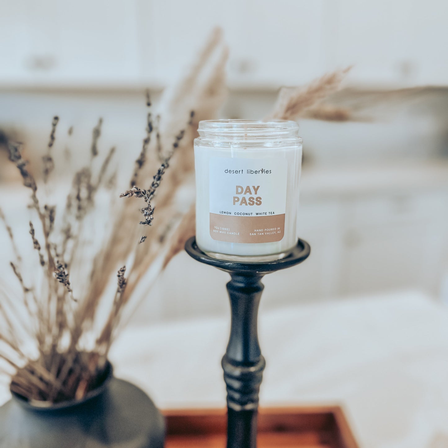 One candle on a black candlestick with dried plants in the background and a blurred kitchen background.