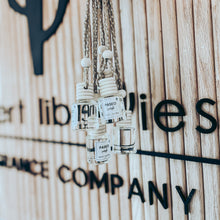 Load image into Gallery viewer, Hand holding multiple small diffuser bottles with visible brand names against a wooden background.