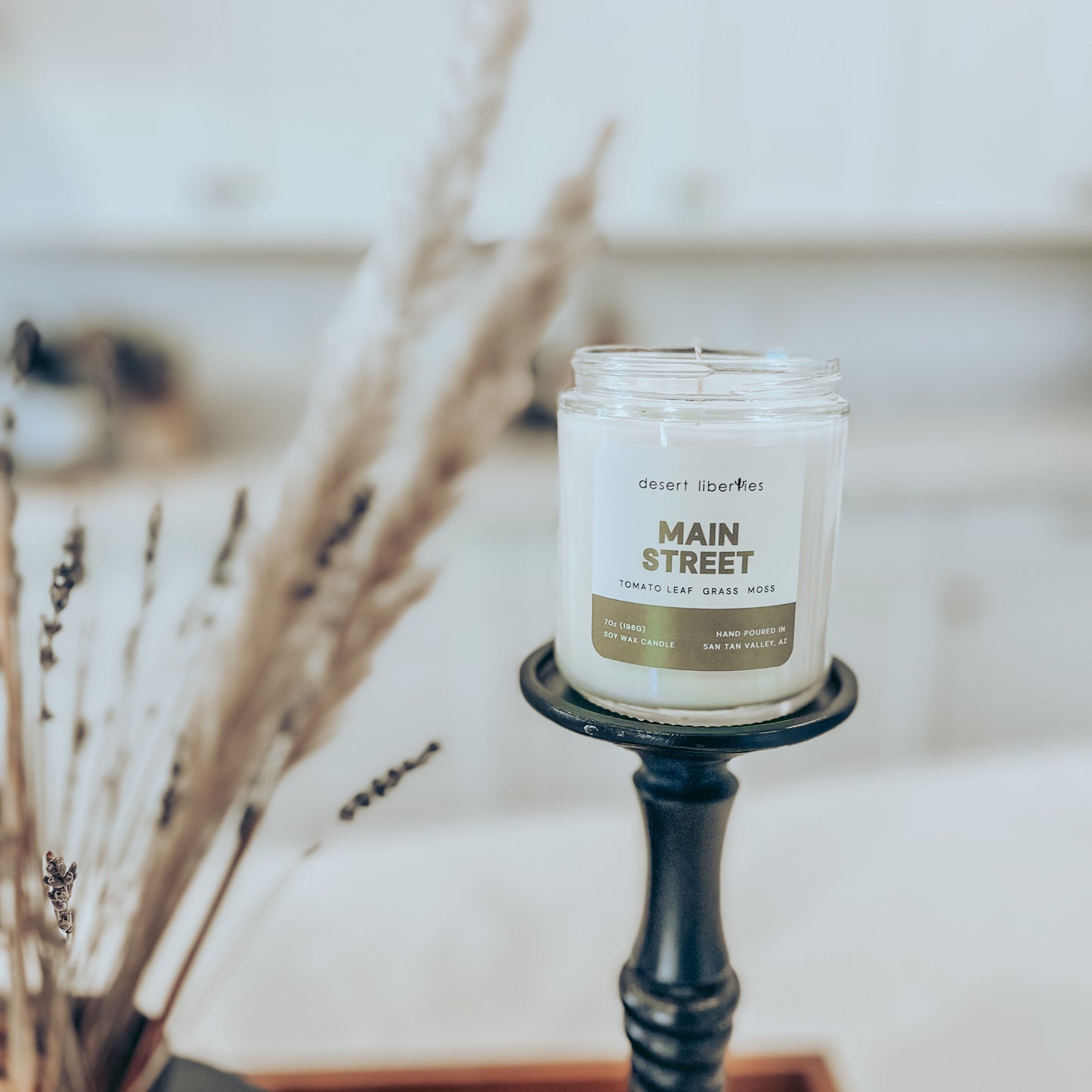 Candle labeled 'Main Street' on a black holder with dried plants in the background