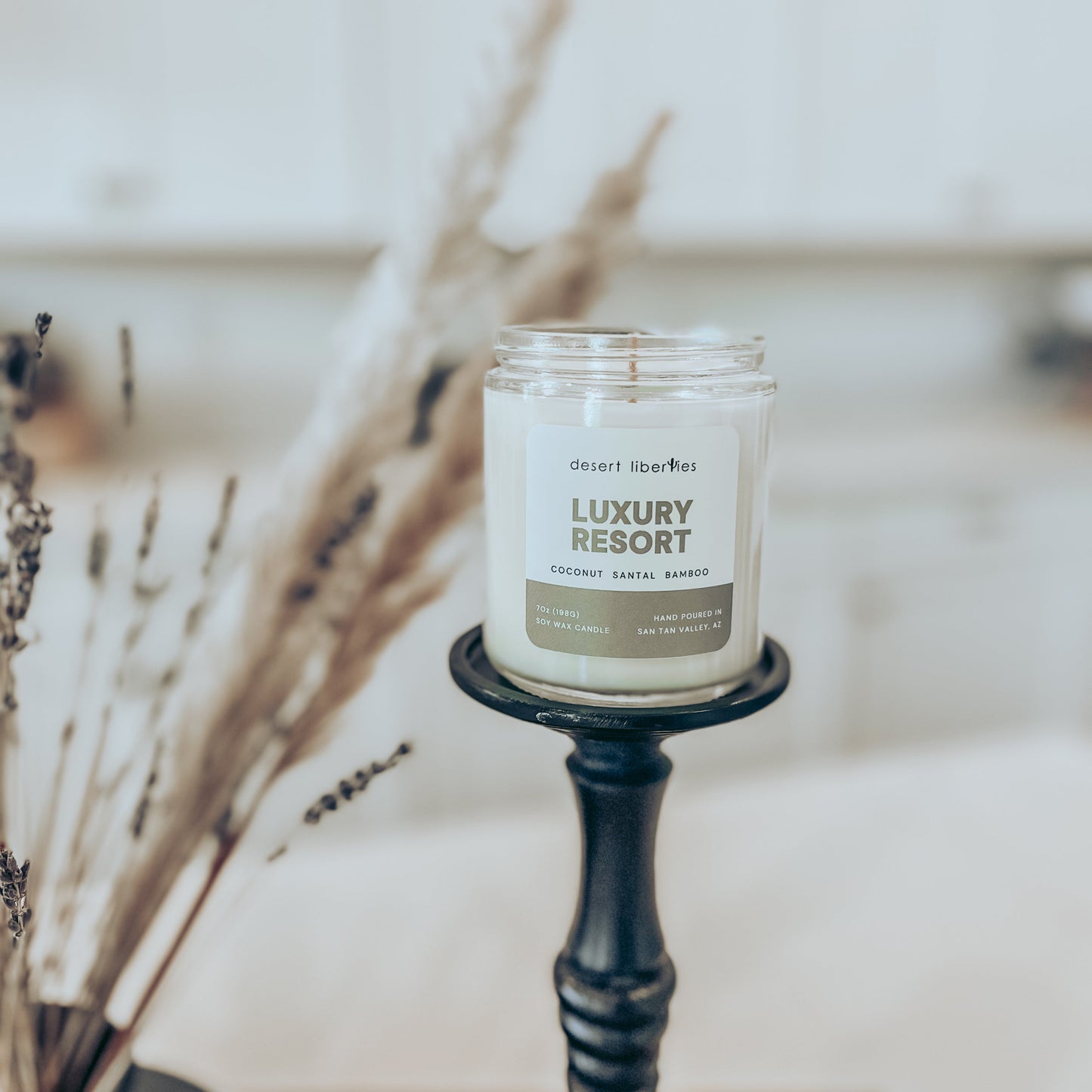 Candle labeled 'Luxury Resort' on a black holder with dried plants in the background