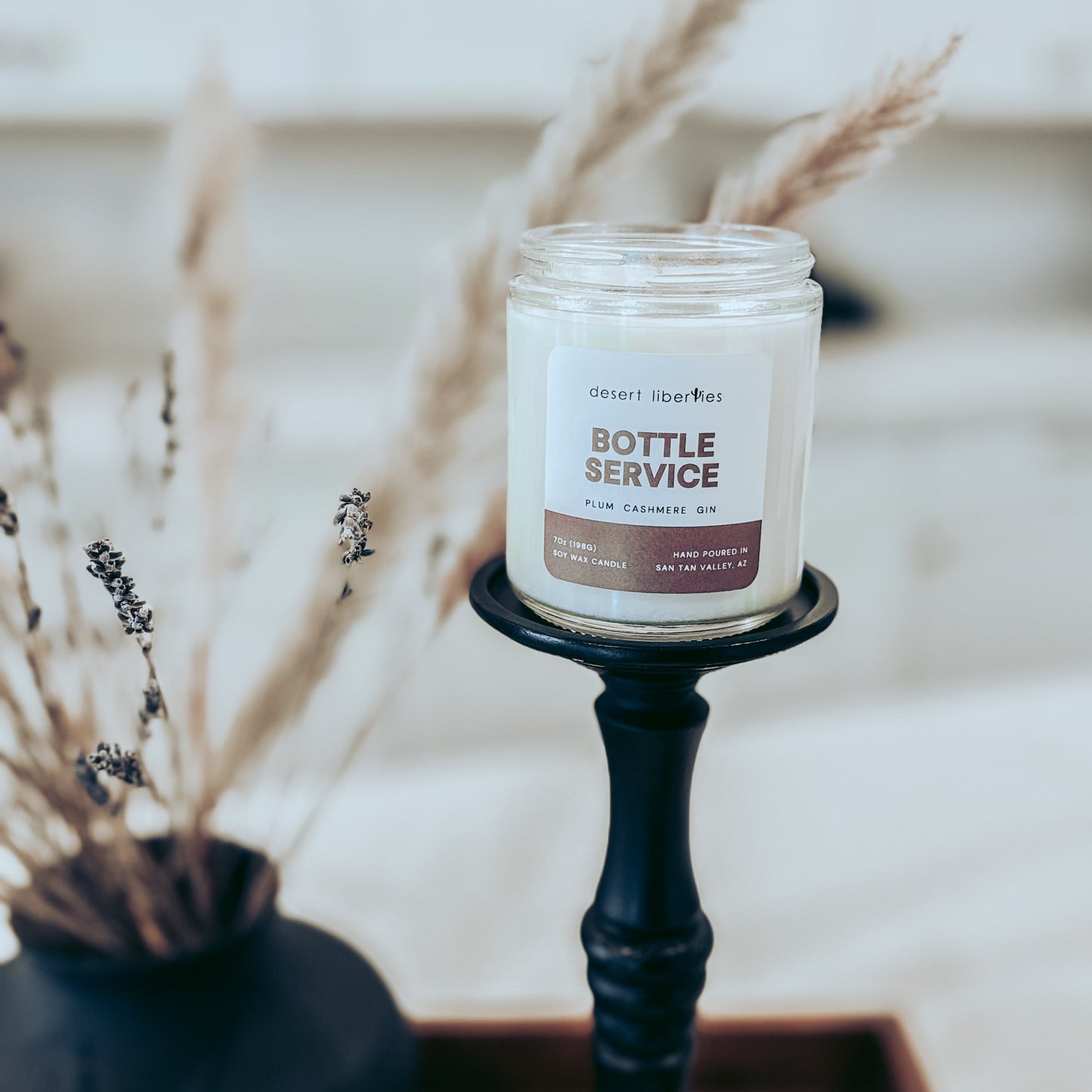Candle labeled 'Bottle Service' on a black holder with dried plants in the background