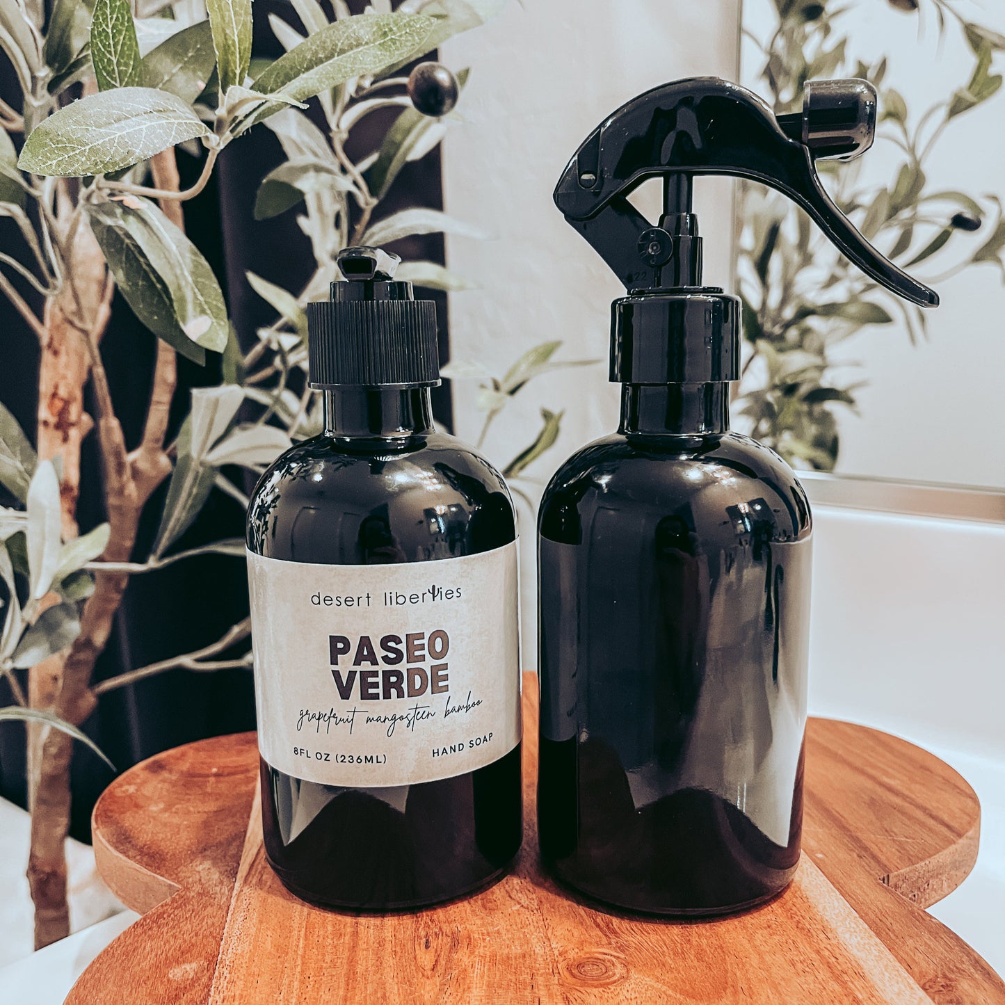 Soap bottle next to an unlabeled spray bottle on a wood surface and olive tree in the background.