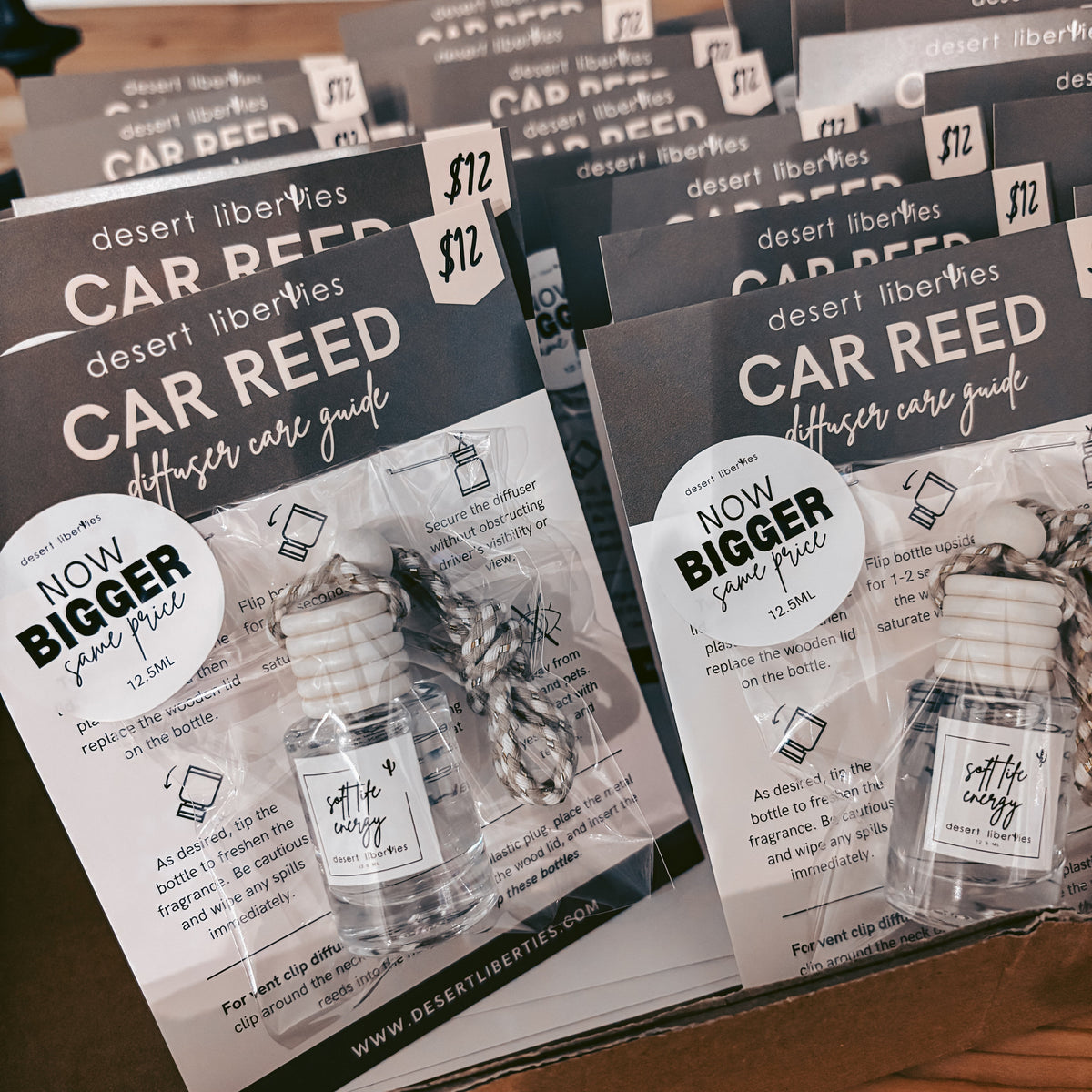 A box filled with multiple copies of a 'Car Reed Officer Care Guide' booklet by Desert Liberates, showing the front cover with a small bottle illustration and a 'Now Bigger' badge.