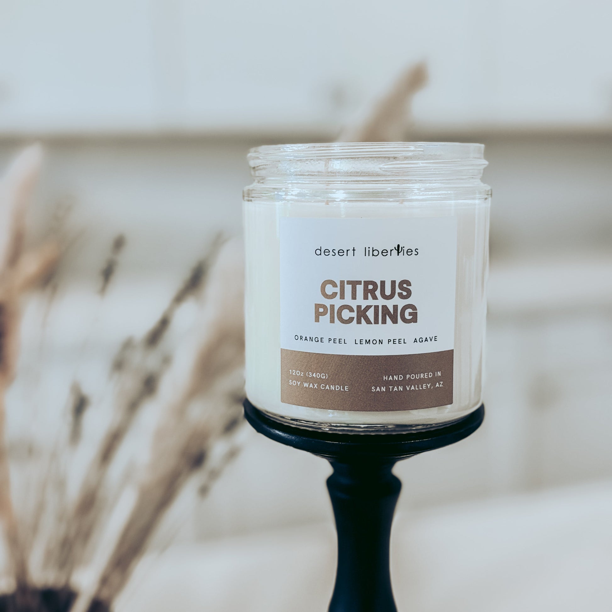 Candle labeled 'Citrus Picking' by Desert Liberties on a black holder with a blurred background.