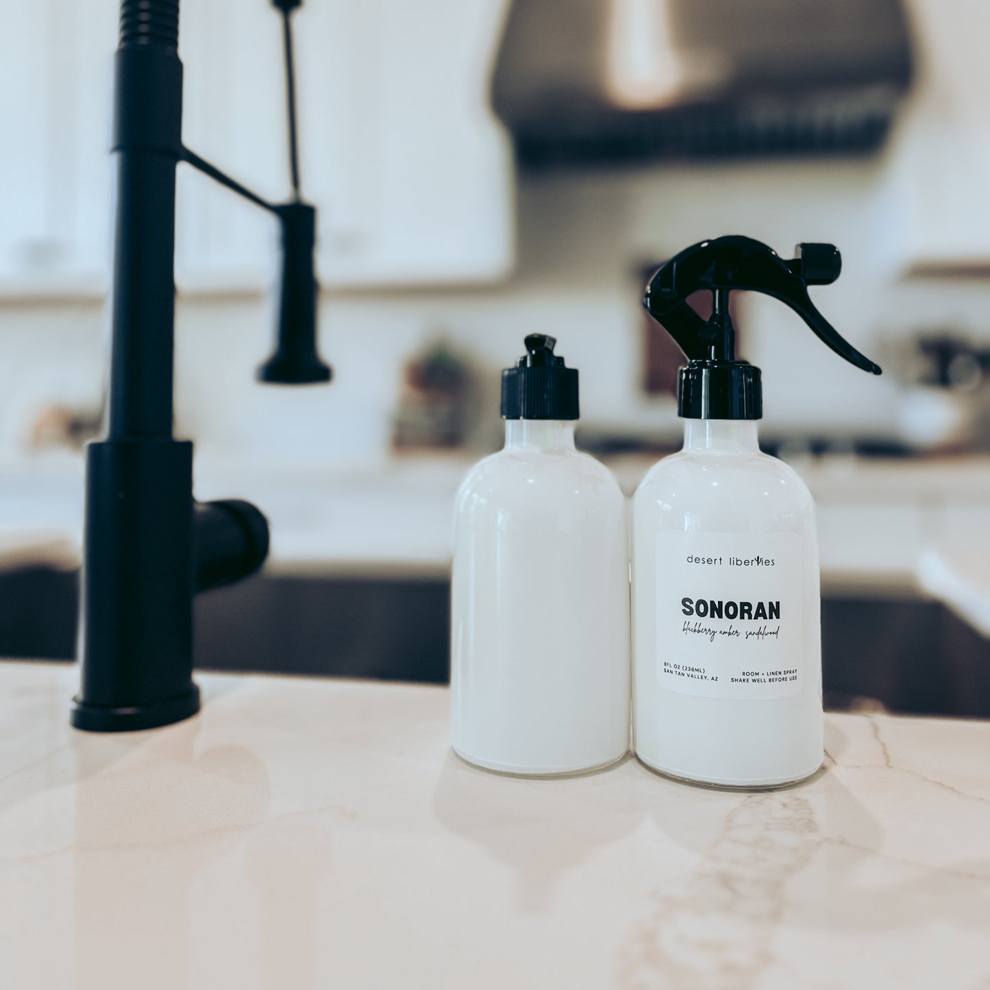 Two white bottles with black sprayers on a kitchen counter.