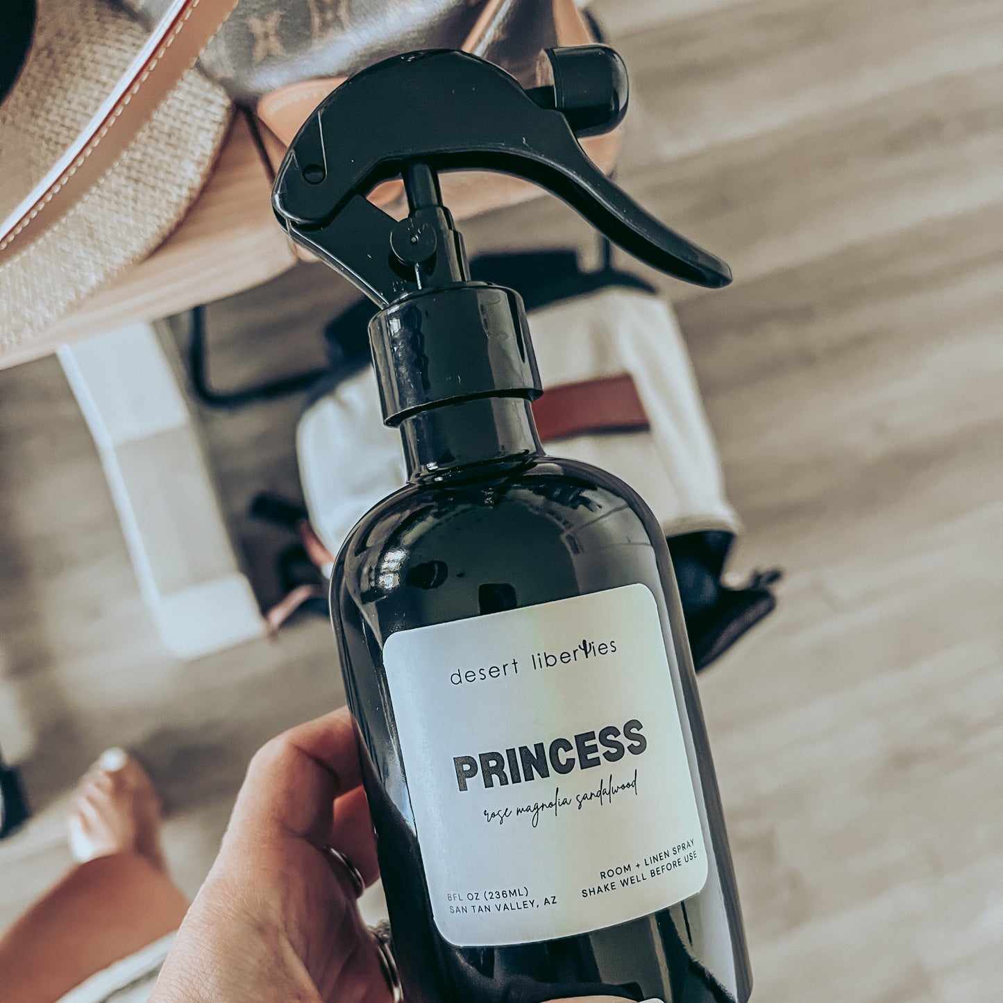 Hand holding a black spray bottle labeled 'PRINCESS' with a blurred background