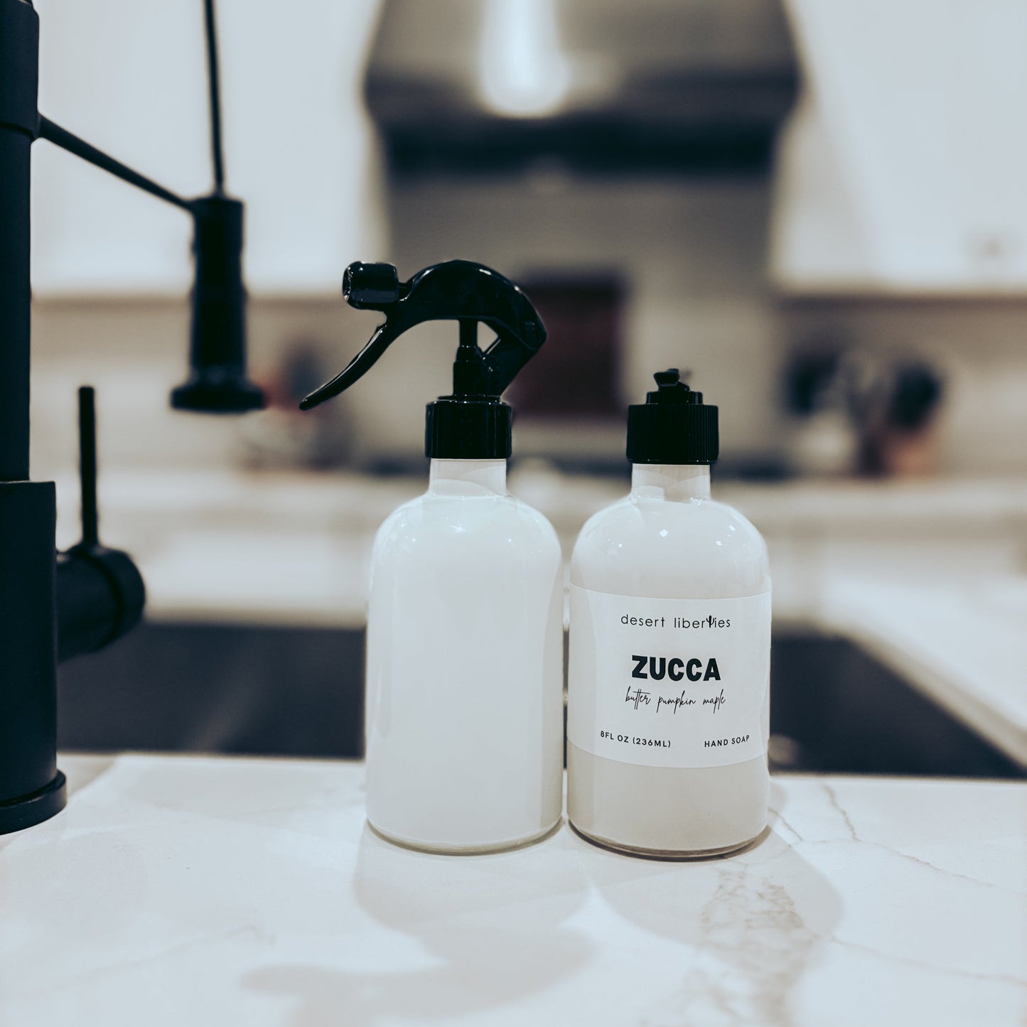 Two white bottles with black nozzles on a kitchen counter.