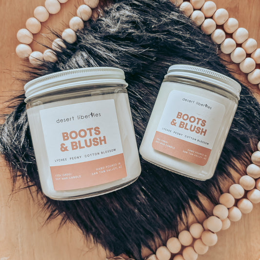 Two 'Boots & Blush' candles on a wooden surface with decorative beads and fur.