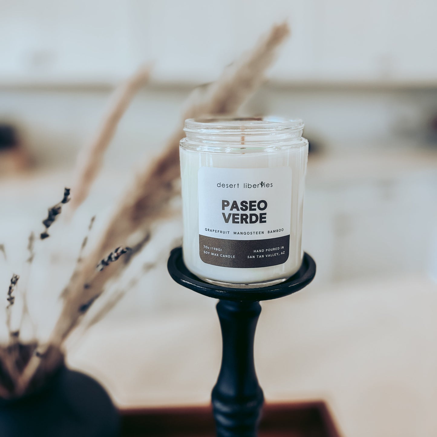 Candle labeled 'Paseo Verde' on a black holder with a blurred natural background