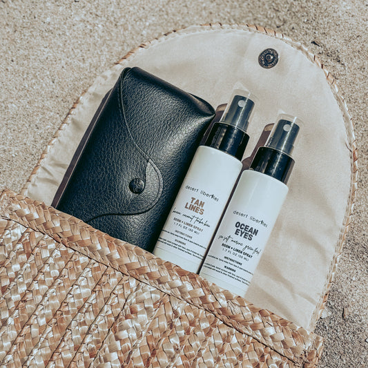 Two spray bottles and sunglasses coming out of woven purse on sand.
