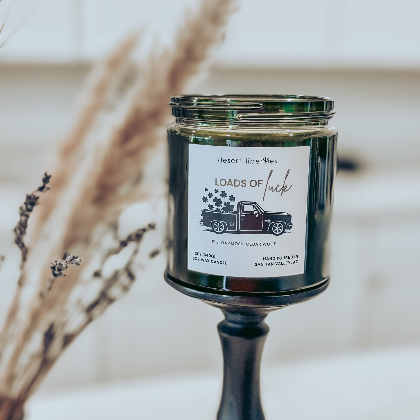 Candle with a label on a stand, surrounded by dried plants