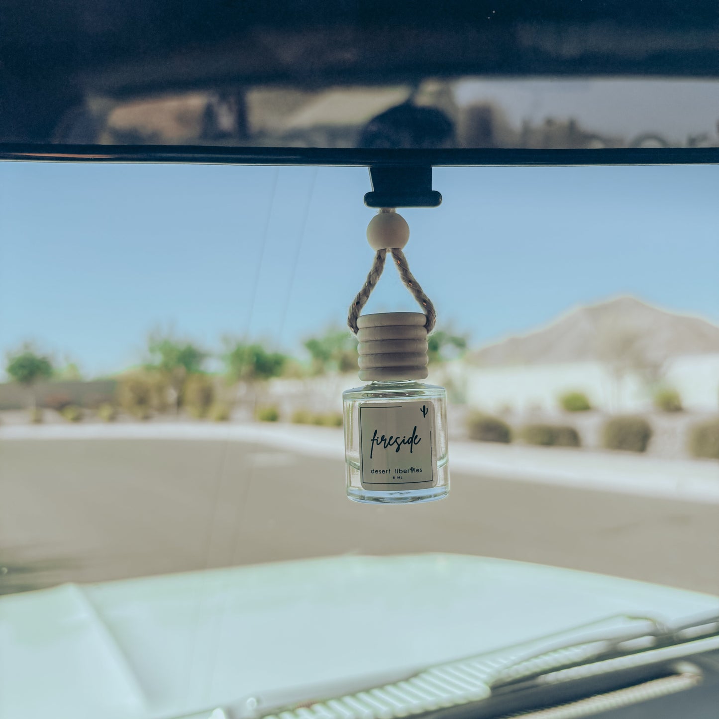 Car air freshener hanging from a car's rearview mirror with a desert landscape in the background.