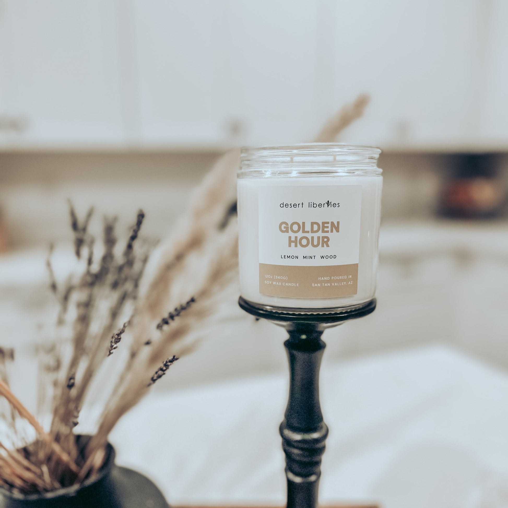 One candle on a black candlestick with dried plants and a blurred kitchen background. 