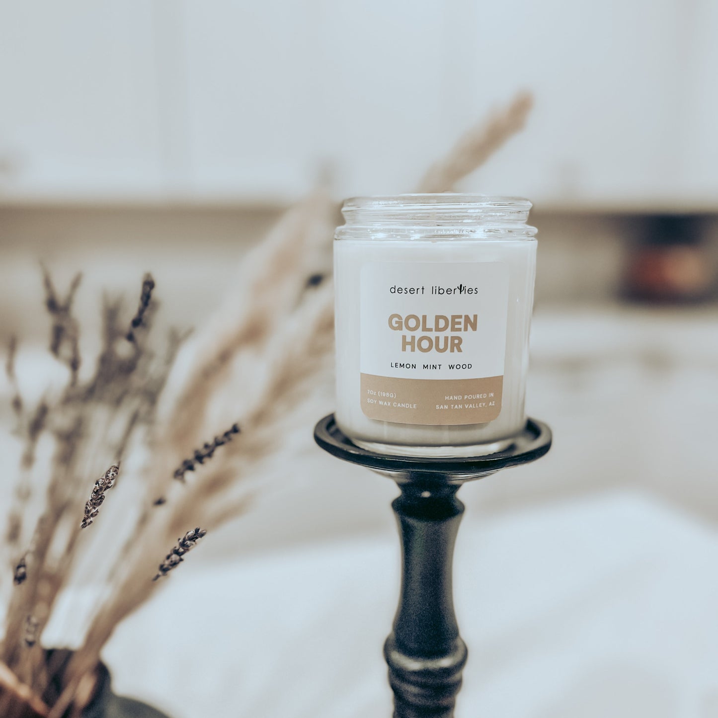 One candle on a black candlestick with dried plants and a blurred kitchen background. 