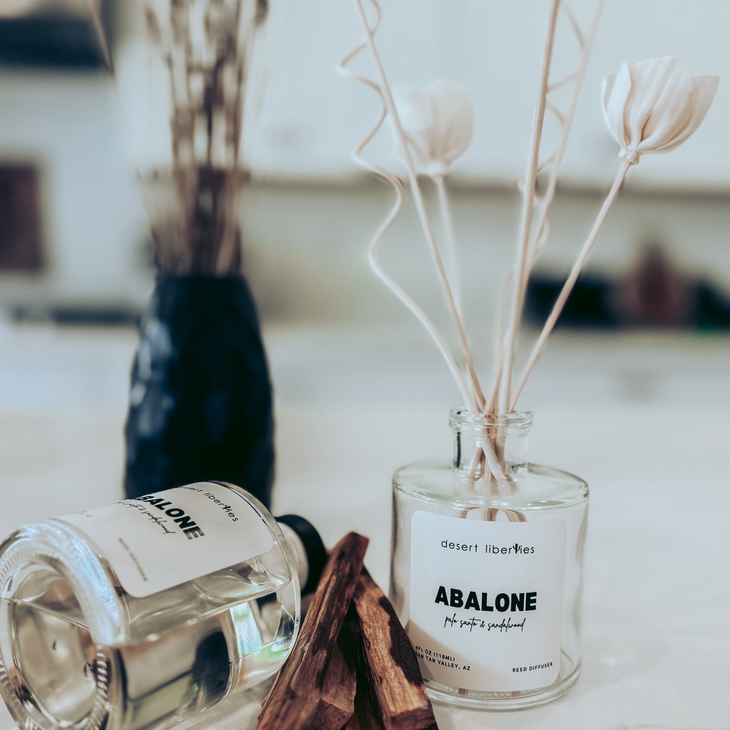 Two glass bottles labeled 'Abalone' with dried plants on a light surface.