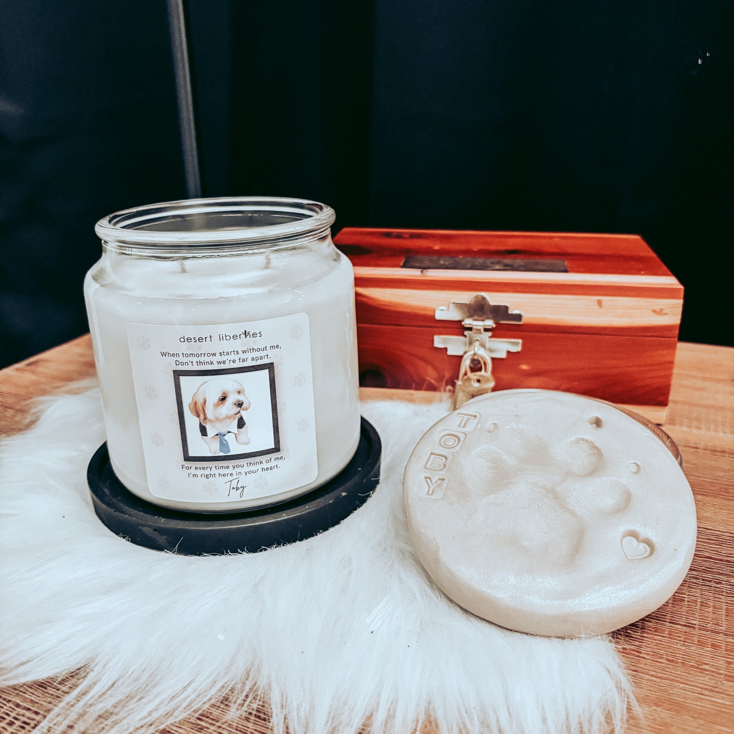 Candle with a label on a wooden surface next to a decorative box and white feathered item.