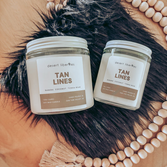 Two jars of 'Tan Lines' product on a fur surface with beads in the background.