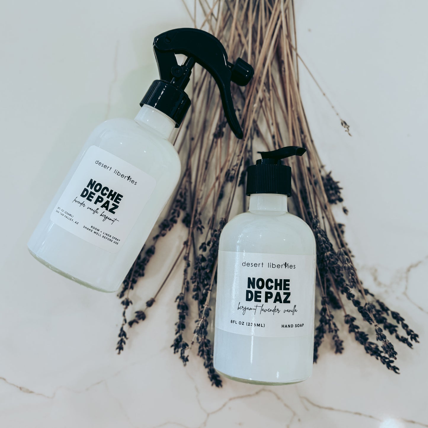 Two bottles of 'Noche de Paz' on a textured surface with dried lavender.