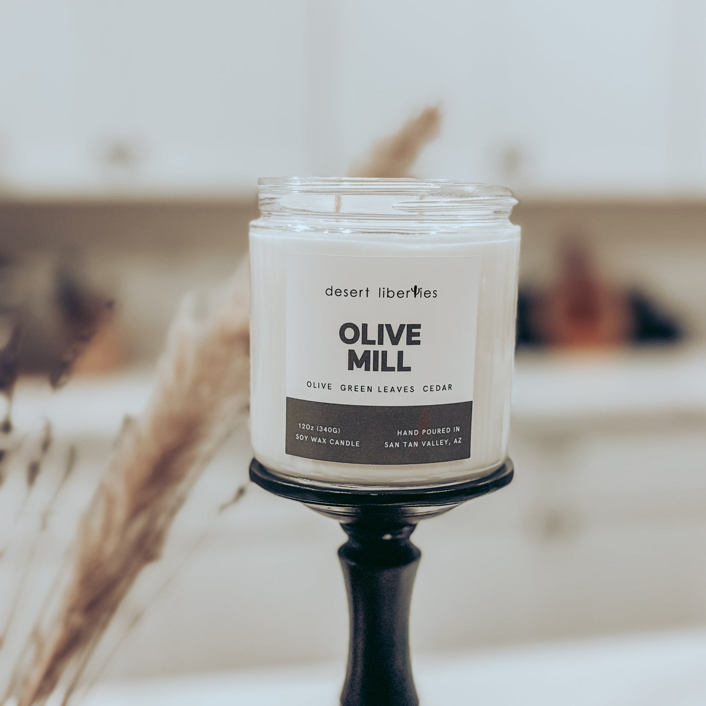 Desert Liberties Olive Mill candle on a stand with a blurred background
