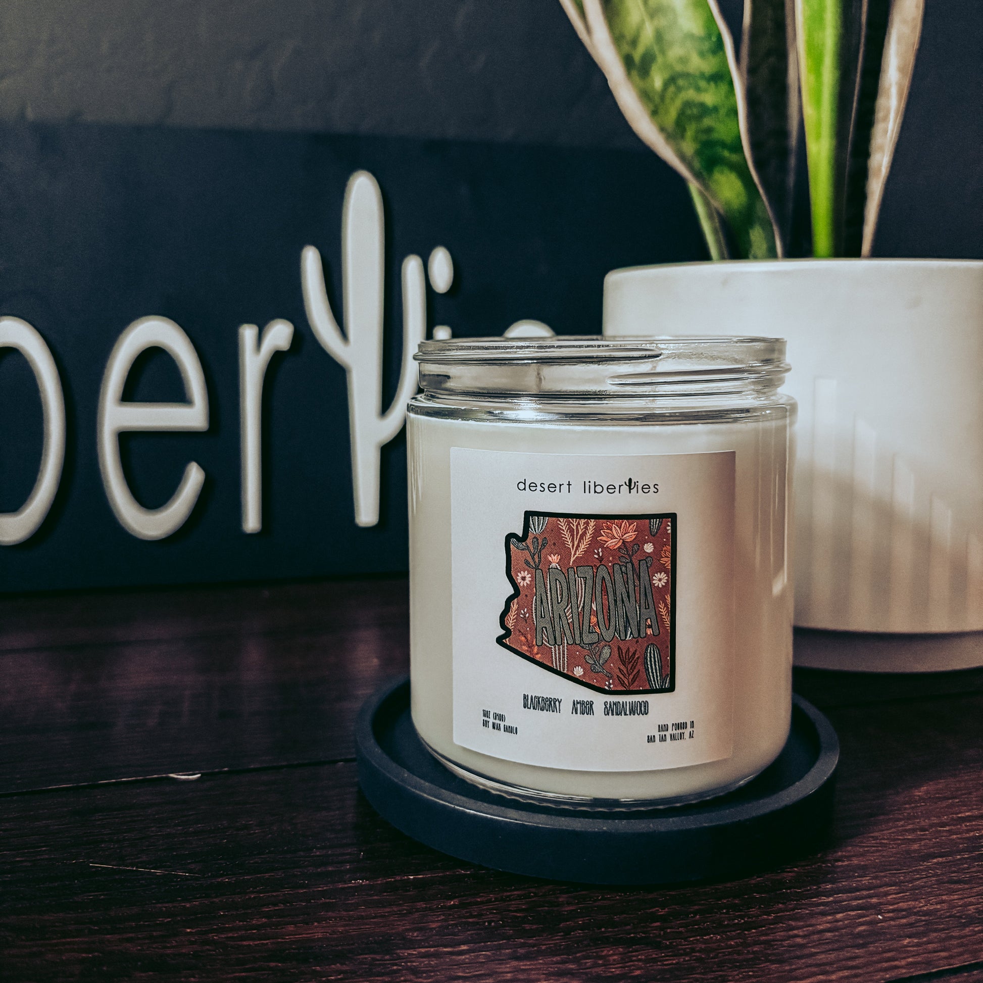 Candle with a label on a dark surface next to a plant