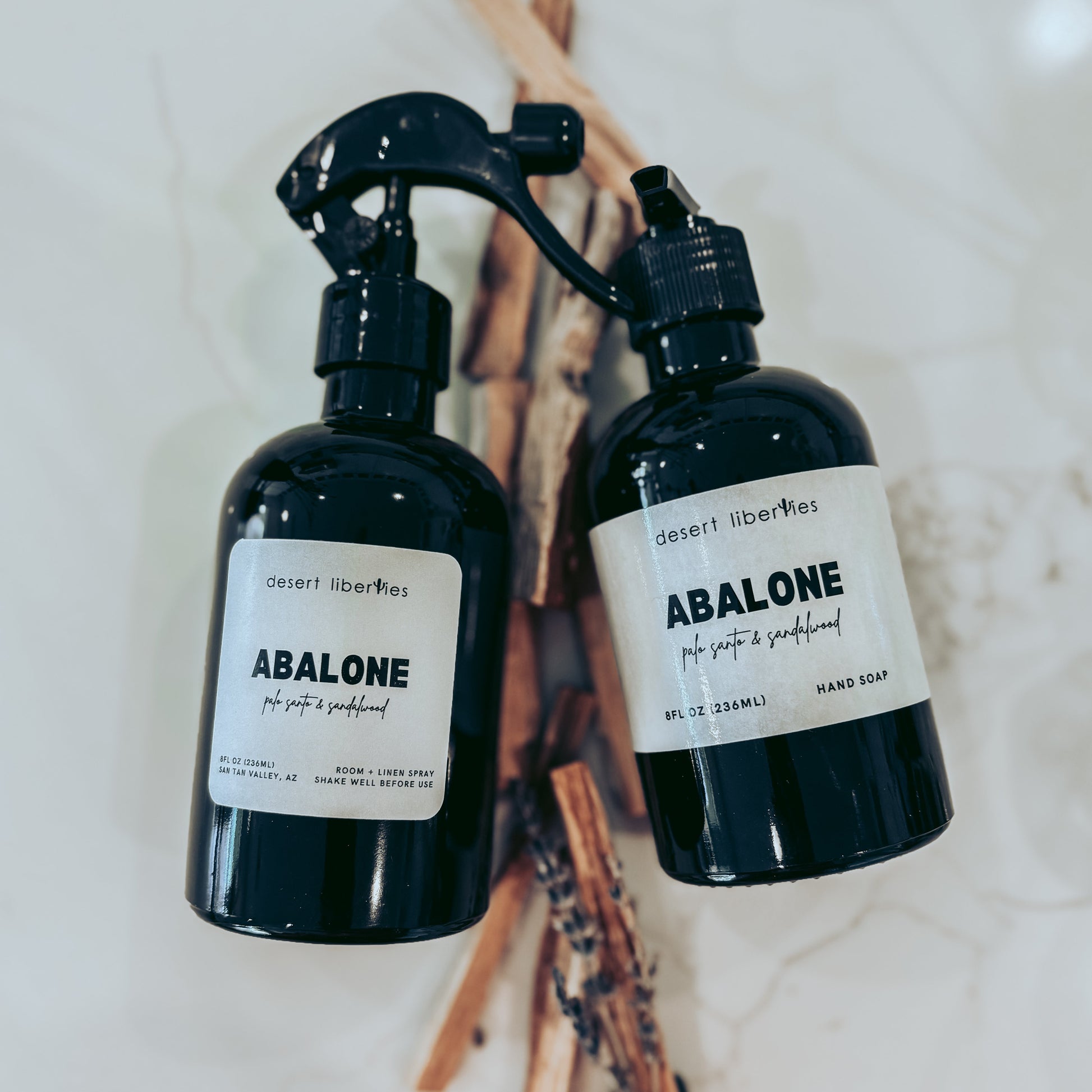 Two black bottles labeled 'Abalone' on a marble surface with palo santo sticks.