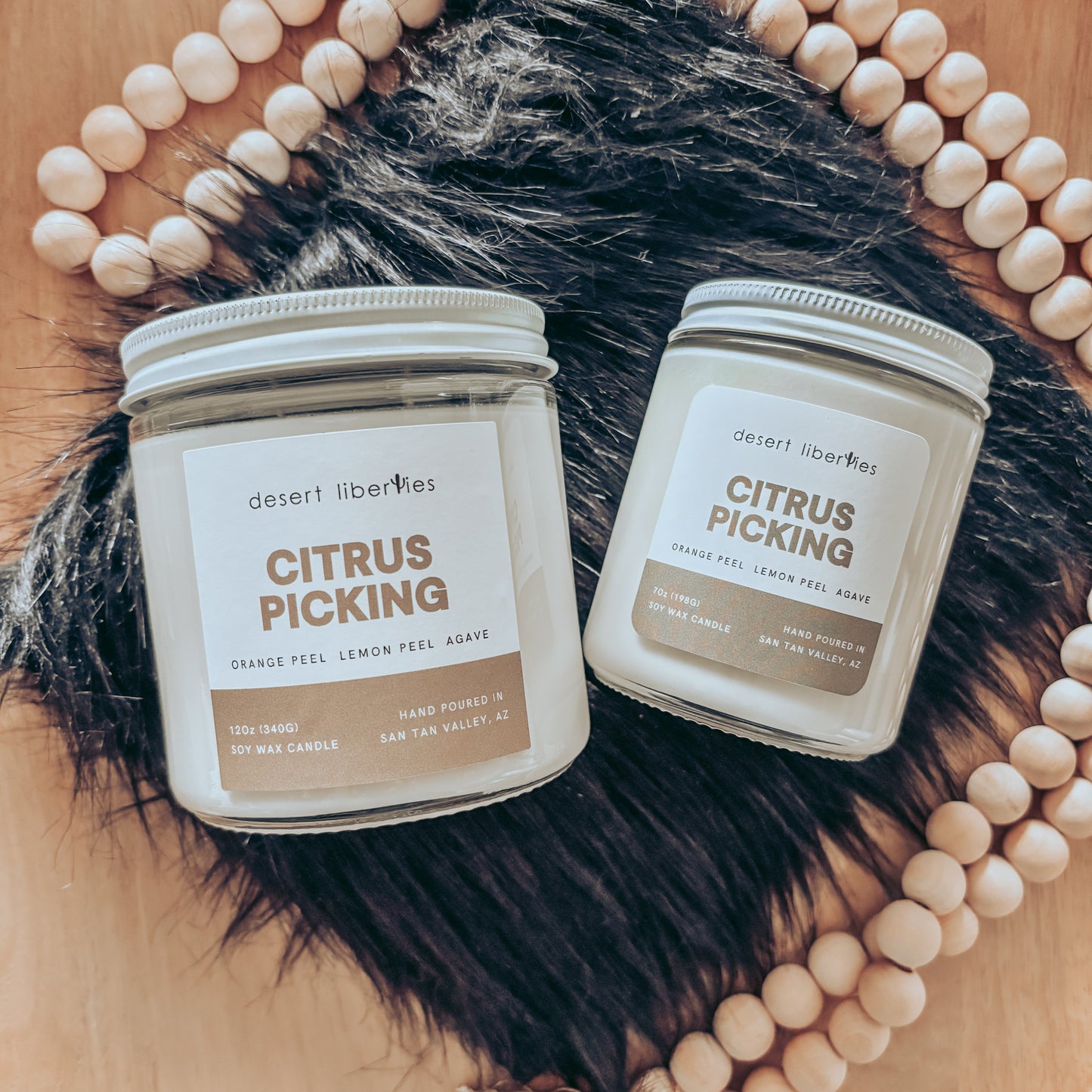 Two candles labeled 'Citrus Picking' on a wooden surface with beads and fur.