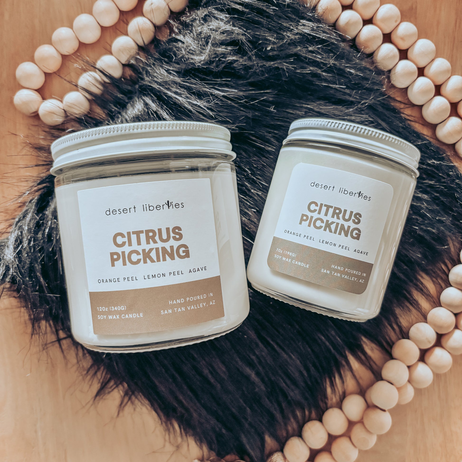 Two candles labeled 'Citrus Picking' on a wooden surface with beads and fur.