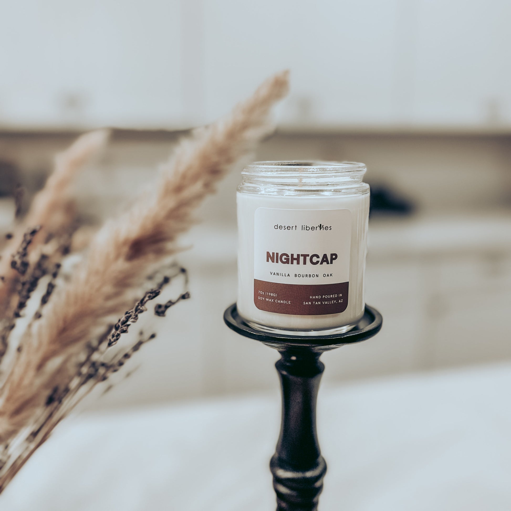 Candle labeled 'Nightcap' on a stand with dried plants and a blurred background
