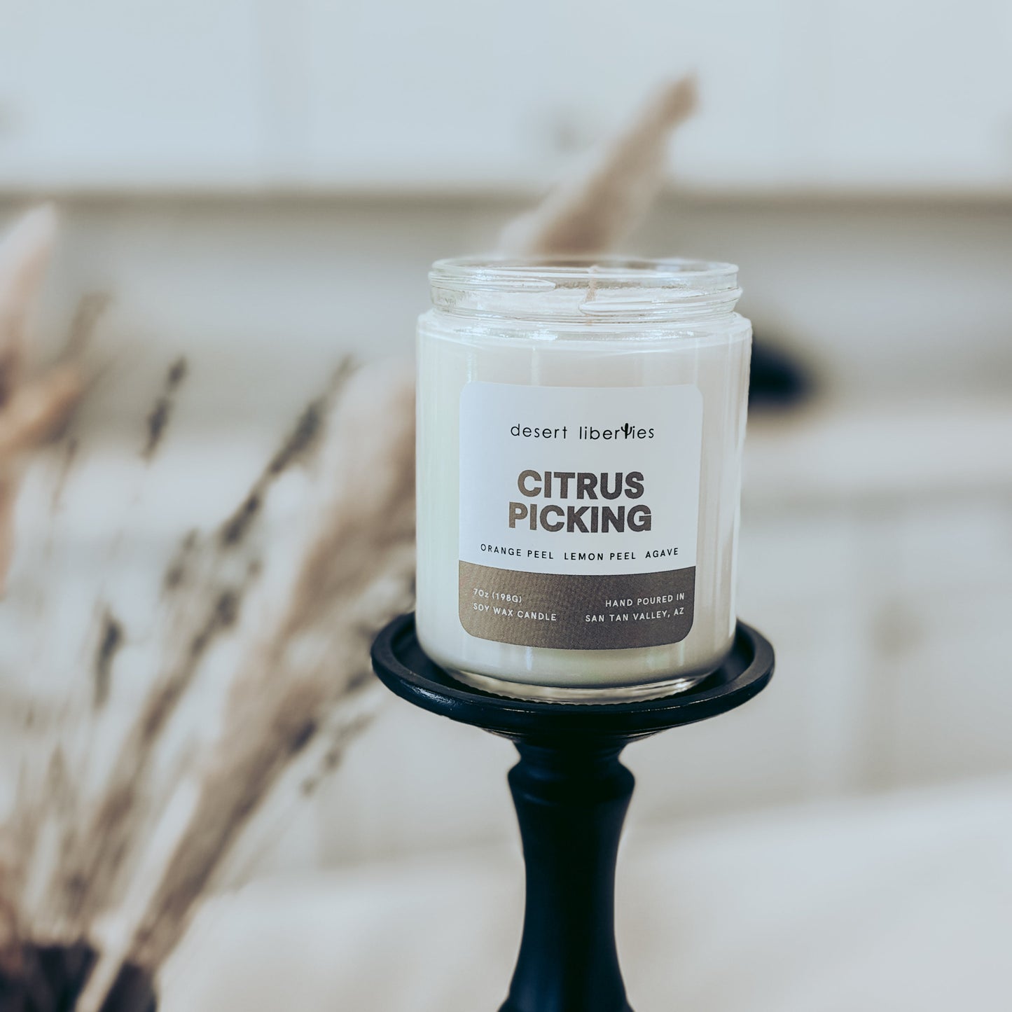 Candle labeled 'Citrus Picking' on a black holder with a blurred background