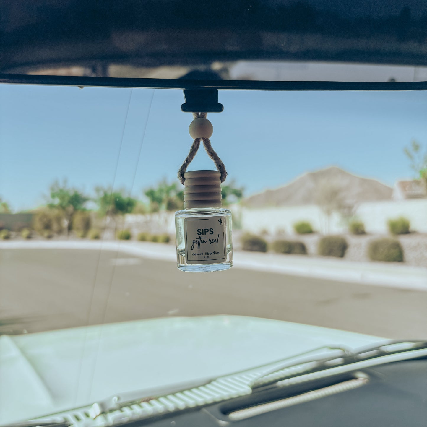 Car air freshener hanging from a car's rearview mirror with a desert landscape in the background.