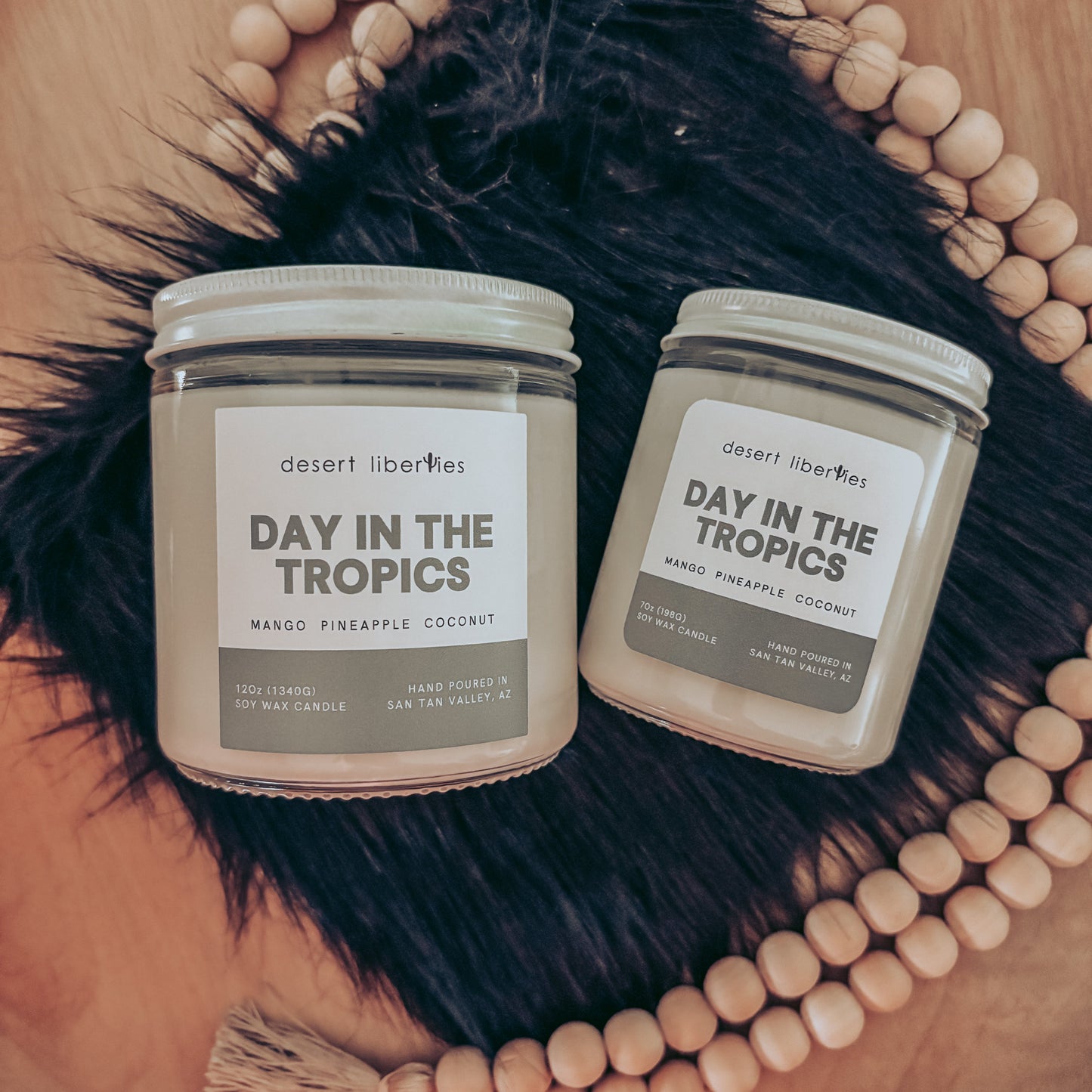 Two candles labeled 'Day in the Tropics' on a decorative background with a hat and beads.