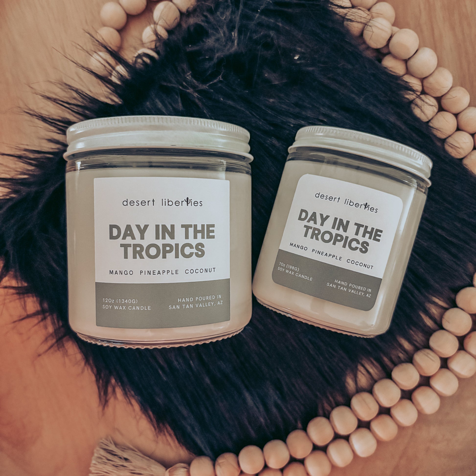 Two candles labeled 'Day in the Tropics' on a decorative background with a hat and beads.