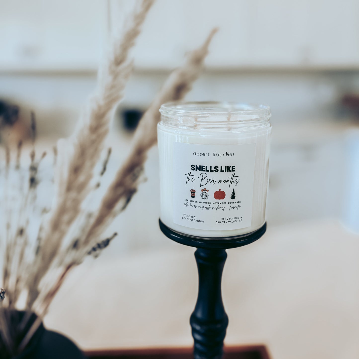 Candle with a label on a stand, surrounded by dried plants