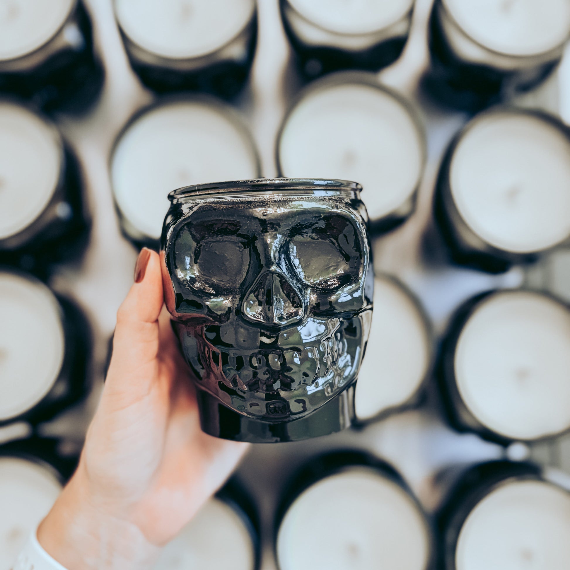 Hand holding a black skull-shaped candle in front of a grid of white candles.