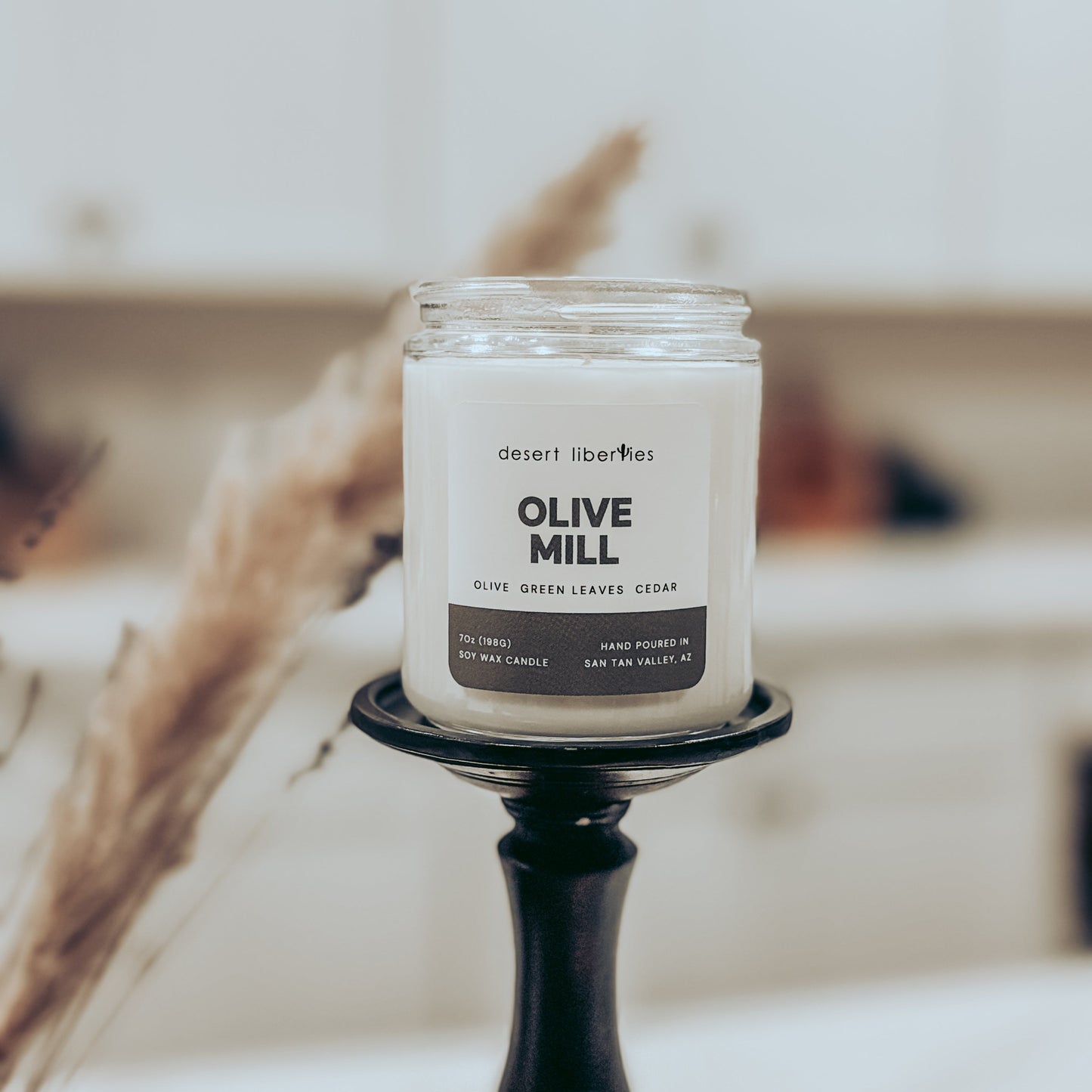 Candle labeled 'Olive Mill' on a stand with a blurred background