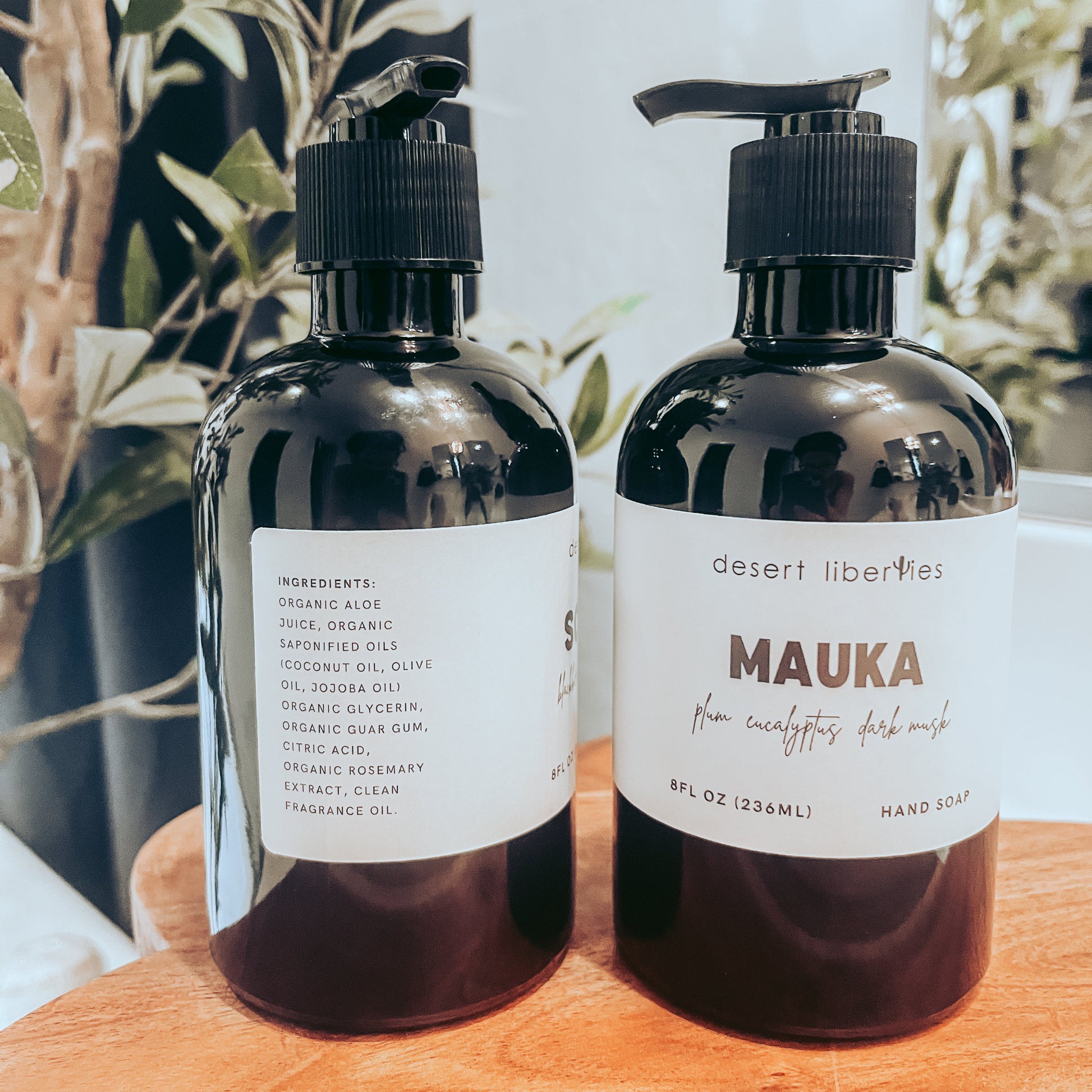 Four reusable glass bottles of organic hand soap with black and white labels, displayed on a marble surface.