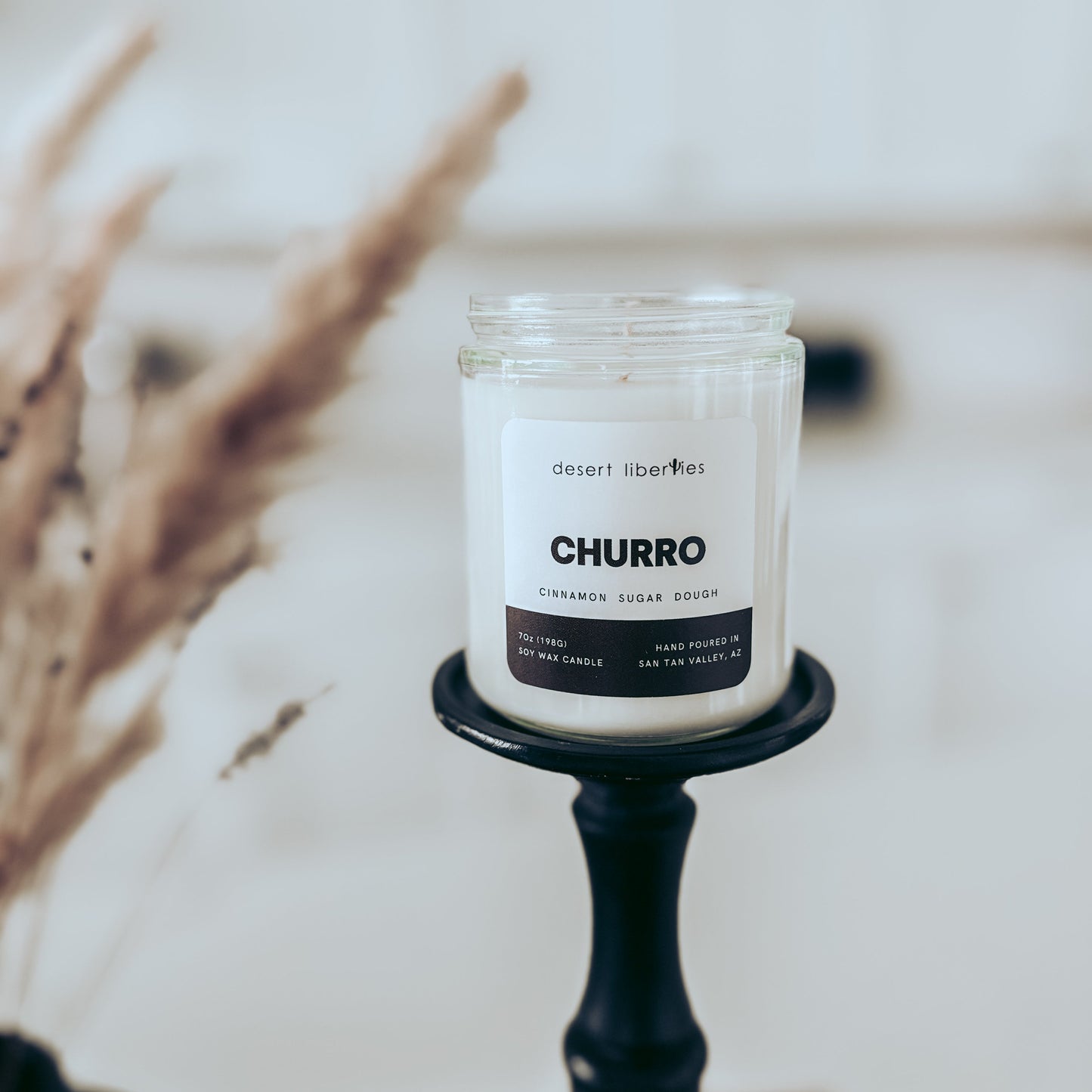 Candle labeled 'Churro' on a black holder with a blurred background